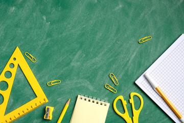 Yellow school supplies on green chalkboard background. Back to school concept.