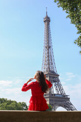 Young girl in red dress sits alone in front of Eiffel Tower in Paris on summer sunny day