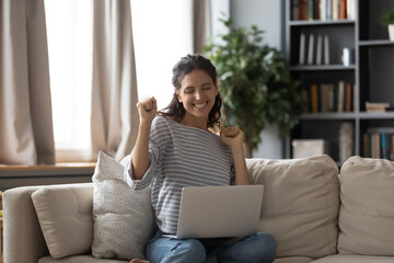 Happy smiling woman looking at laptop screen, celebrating success, sitting on cozy couch in living room, overjoyed girl reading email with good news, received great shopping sale offer