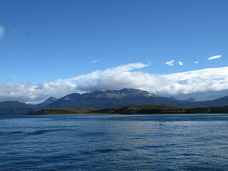 View of Tierra del Fuego (Land of Fire) and the Beagle Channel - blue water, flock of birds and white clouds over mountain peaks, Argentina 