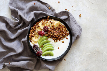 Bowl of homemade granola with fresh berries, banana, kiwi, and yogurt on white background. Top view with negative space 