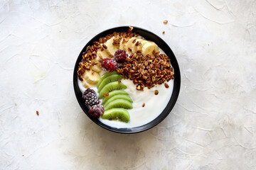 Bowl of homemade granola with fresh berries, banana, kiwi, and yogurt on white background. Top view with negative space 