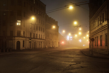 An empty illuminated asphalt road through the old historical buildings and houses in a fog at...