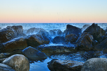 Waves break on the rocks on the beach creating splashes at sunset