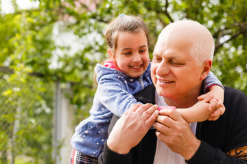 Fototapeta premium Portrait of small girl with senior grandfather in the backyard garden, standing.