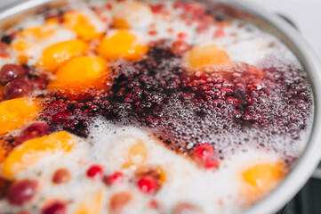 Fresh fruits: apricots, cherries, raspberries, apples are boiled in boiling water in a metal pan on a stove with bubbles and foam close-up. Cooking delicious homemade compote. Photography, concept.