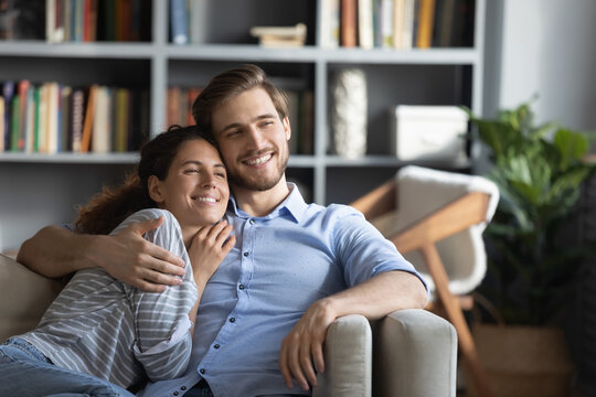 Smiling Dreamy Young Couple Hugging, Relaxing On Couch In Living Room At Home, Happy Beautiful Woman And Man Cuddling, Dreaming About Good Future, Planning, Enjoying Lazy Weekend Together