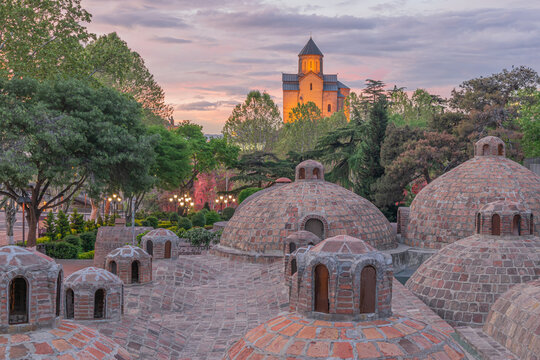 Cityscape of the historic Old Tbilisi with famous sulphur baths, illuminated Metechi Church and little green park in the evening. Tbilisi, Georgia