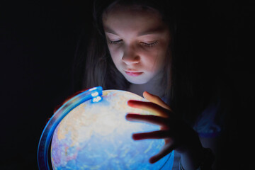 Little girl looking in the dark at an illuminated earth globe