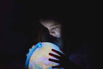 Fototapeta premium Little girl looking in the dark at an illuminated earth globe
