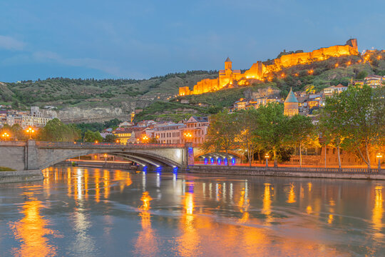 Cityscape of illuminated historic old Tbilisi with ancient Narikala fortress, Sioni Cathedral,  Metechi stone Bridge over the Mtkvari/Kura river and  mosque in the evening. Tbilisi, Georgia