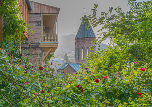 Cityscape of Tbilisi with traditional wooden balconies, blooming roses, orthodox church and TV Broadcasting Tower during the colorful sunset. Tbilisi, Georgia 
