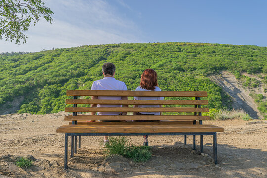 Young couple sitting on the wooden bench under the tree shadow and enjoying the sunny day. Tbilisi, Georgia 