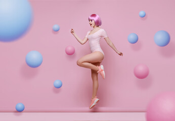 Woman with purple hair in trendy sportswear jumping. Smiling beautiful slim brunette girl in fashion lingerie expressing happy emotions on bright trendy pink background. Free space for text.