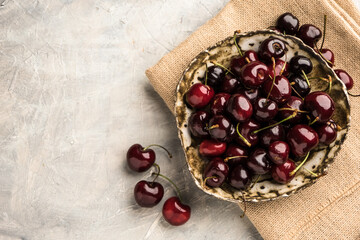 Ripe sweet cherry in ceramic bowl at concrete background