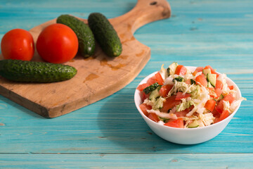 Vegetarian salad of fresh vegetables with olive oil in a white Cup on a blue wooden table. Tomatoes, cucumbers are on the cutting Board