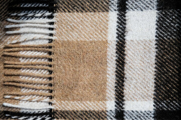 Fototapeta premium Brown plaid blanket with long edges. Close up view of a full background. Textile in interior design. Warming up cozy material to cover up when studying or working from home in isolation. Fall vibes.