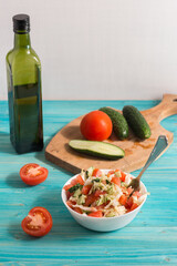 Cooking a vegetarian salad of fresh vegetables with olive oil on a blue wooden table. Light summer dinner