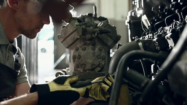 Auto Mechanic Working On Bus Engine Using Hand Screwdriver To Tighten Parts Of Mechanism. 