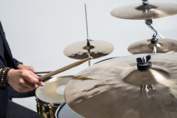 Close up of hands of male drummer holdning drumsticks sitting and playing drums on white background