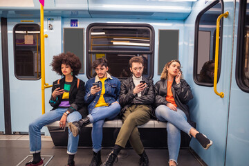 Group of friends using smartphones while traveling by metro