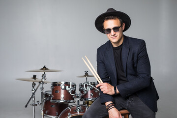 Young man drummer behind drum set and plays the drums in studio background