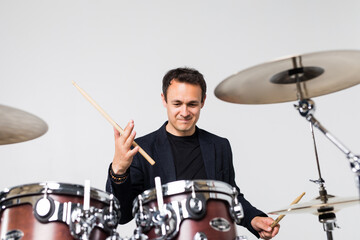 Fototapeta premium Young man play with drumsticks sitting at drums isolated on white background