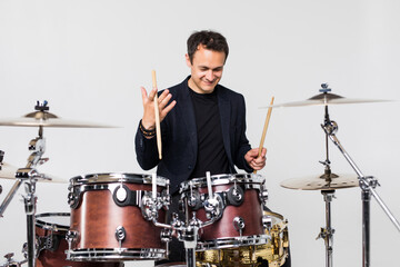 Young man play with drumsticks sitting at drums isolated on white background