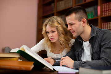 Two students guy and girl interested study the material from the book and prepare for exams in the library.