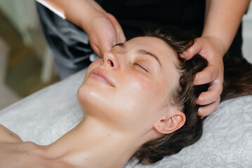 Fototapeta na wymiar A young pretty girl is enjoying a professional head massage at the Spa. Body care. Beauty salon