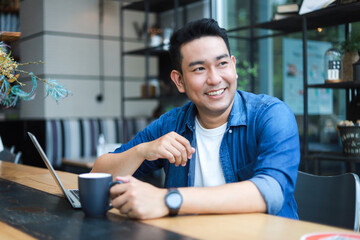 Young Asian Man in blue shirt working with laptop in coffee shop cafe smile and happy face