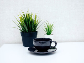 on a light table there is a black Cup with a mug, and in the background two flowers in a pot