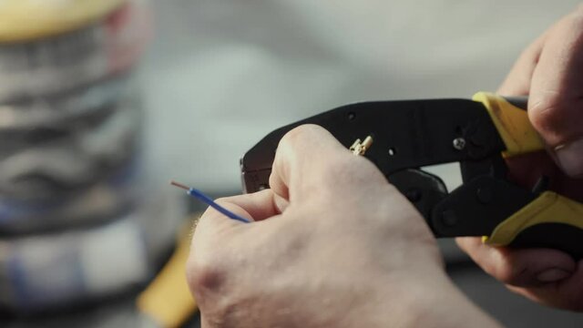 skilled technician puts small connectors to bright color thin wires using crimping tool on blurred background in workshop close view