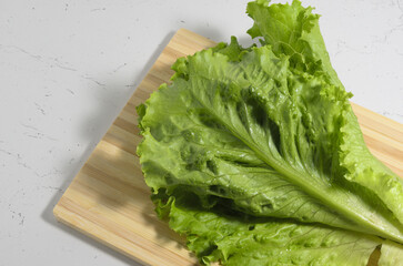 Green lettuce leaf on cutting board and texture table top on the background. Selective focus.