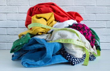 A jumble of multicolored clothing and a measuring tape on a neutral background in close-up....