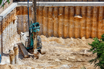 A heavy excavator in conjunction with a drilling rig works to strengthen the foundation of the future high-rise building.