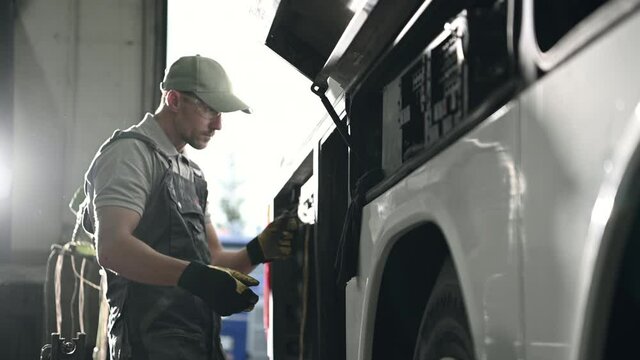 Male Repairman Checking Electrical Wiring And Connections In Large Commercial Bus. 