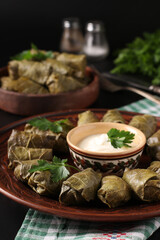 Stuffed grape leaves - traditional Mediterranean cuisine, Dolma on a brown plates with fresh parsley and garlic sauce on a black background, Closeup, Vertical format