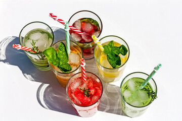 Iced summer drink. Refreshing multicolored alcol-free cocktails in glasses with straws. Watermelon,cucumber, lemon, orange, strawberry cocktail on white background. Top view. Space for text.