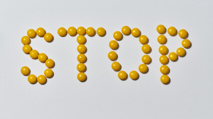Word STOP made from yellow medical pills on light background. Stop disease. Health care and treatment concept
