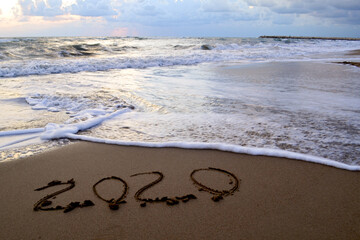 The year 2020 is drawn on sand with foam waves