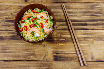 Bowl of instant Chinese noodles with shrimps, green onion and red hot chilli peppers on wooden table. Top view