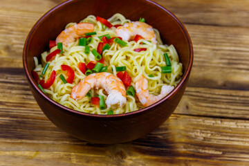 Bowl of instant Chinese noodles with shrimps, green onion and red hot chilli peppers on wooden table