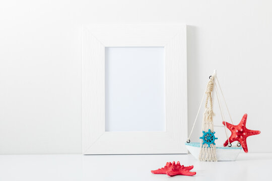 Summer composition. Travel concept. White frame mockup in interior with sea elements on white wall background. Template frame for text. Poster mockup.