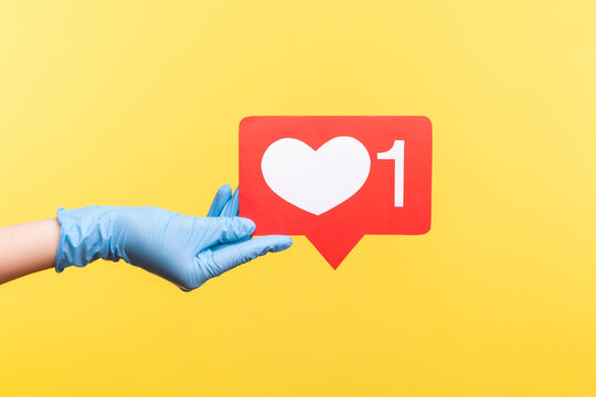 Profile side view closeup of human hand in blue surgical gloves holding social media like stick. indoor, studio shot, isolated on yellow background.