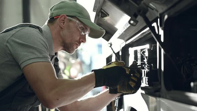 Skilled Auto Technician Checking And Replacing Fuse In Panel Of Bus In Automotive Service Center. 