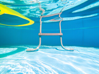 Underwater view of a grey pool ladder and a yellow air mattress