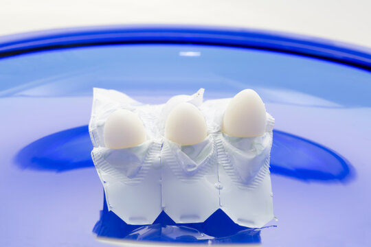 Chemical barrier contraception. Three sperm-killing suppositories in half-peeled suppository shells on blue background