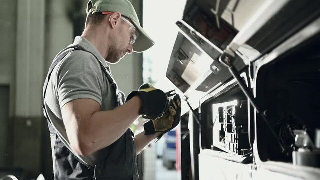 Auto Mechanic Opens Hood Of Vehicle Electric Panel And Checks Fuse Connection In Electrical Box. 