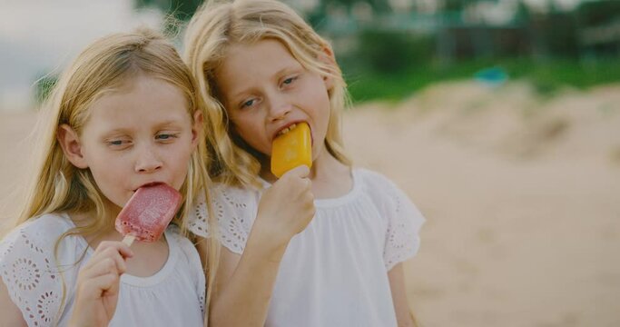 Happy young girls laughing and eating ice cream on the beach, summer family lifestyle